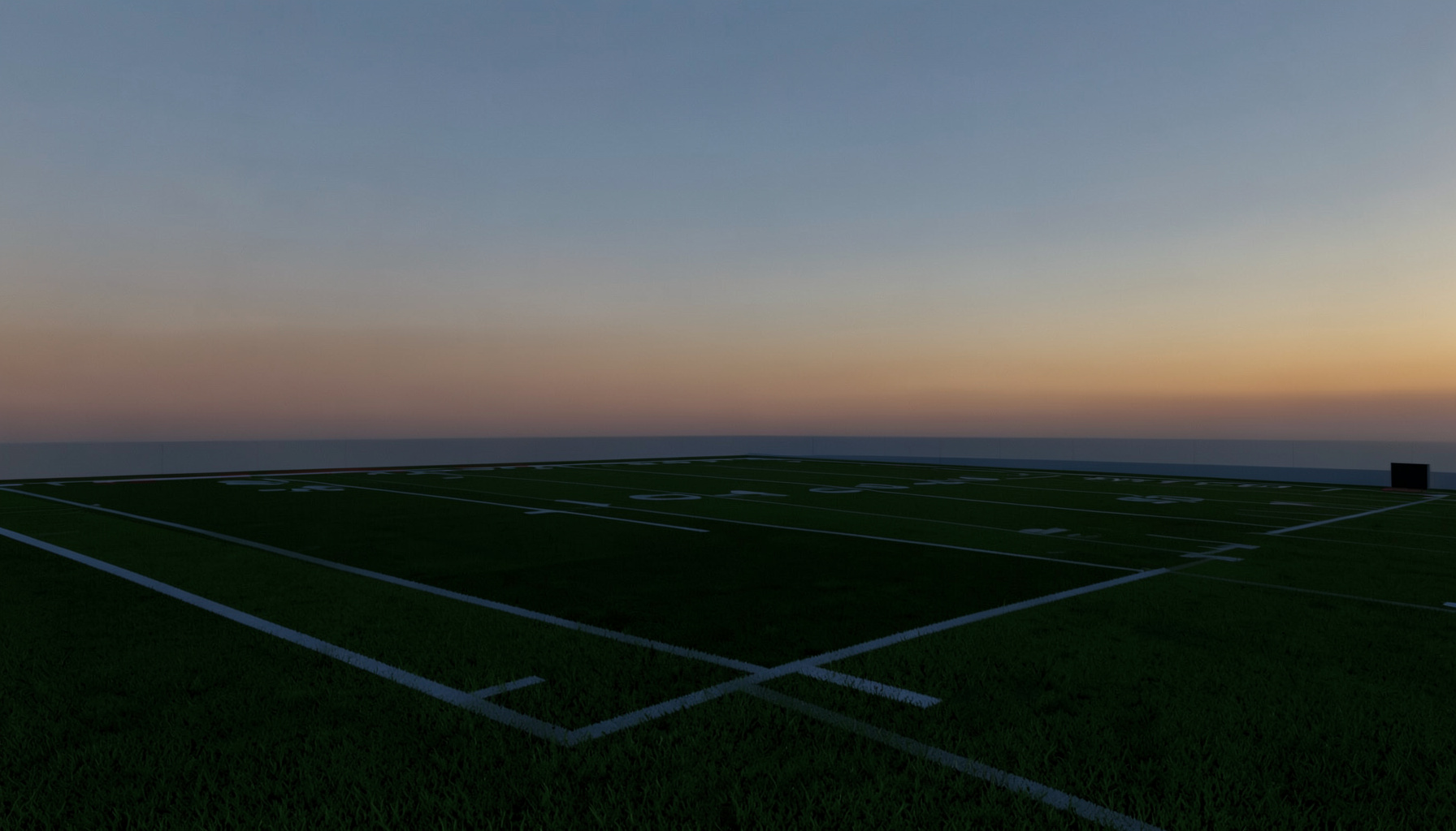 A football field at dusk under a wide sky, with deep green turf and soft amber light fading across the horizon